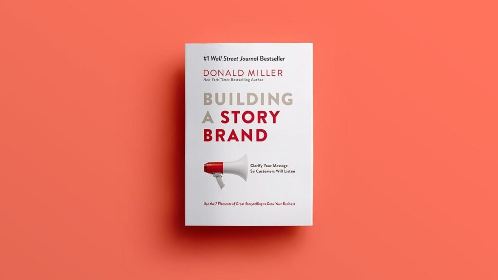 The book cover of Building a StoryBrand by Donald Miller. The design features a white background with bold red and beige text. The title, 'BUILDING A STORY BRAND,' is prominently displayed, accompanied by a red megaphone graphic. The subtitle reads 'Clarify Your Message So Customers Will Listen,' and the bottom section encourages using the 7 elements of storytelling to grow your business.